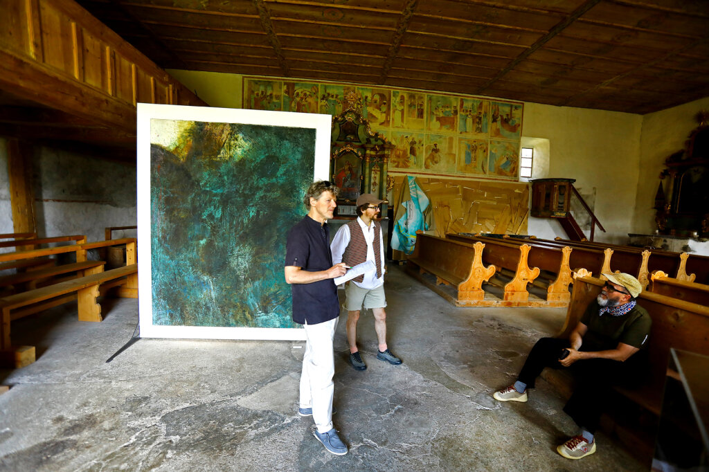 Markus Larcher war in der vergangenen Woche im Vinschgau unterwegs und hat bei der Ausstellung +/-Folk (in zwei Bunkern und einer Kirche) viel Kunst genossen: Kurator Daniel Costa (mit Weste) und Initiator Othmar Prenner (sitzend) erklären, was das Konzept der Ausstellung ist, im Hintergrund ein Bild von Jörg Hofer. Foto: Alexander Alber